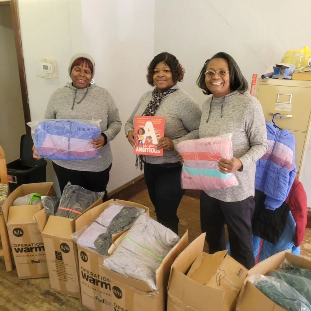 The Founder of Literacy and More with two community members holding books and coats for an event.